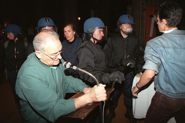 Le père Henri Coindé (g), curé de l'église Saint-Bernard à Paris, se tient devant l'autel, lors de l'intervention, le 23 août 1996 des forces de l'ordre, pour évacuer les 300 africains sans-papiers, réfugiés dans cette église depuis une cinquantaine de jours.