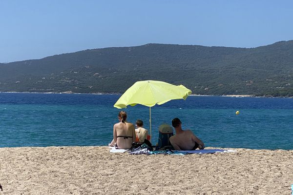 Une famille de touristes sous un parasol dans le sable regardent la mer sur une plage à Propriano.